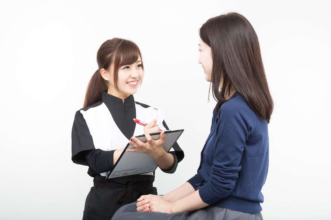 クリップボードを持ったスタッフが女性と話している様子