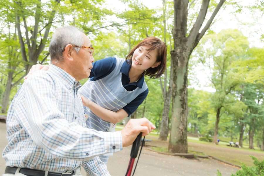 公園で、杖をついて歩く男性に付き添うスタッフ